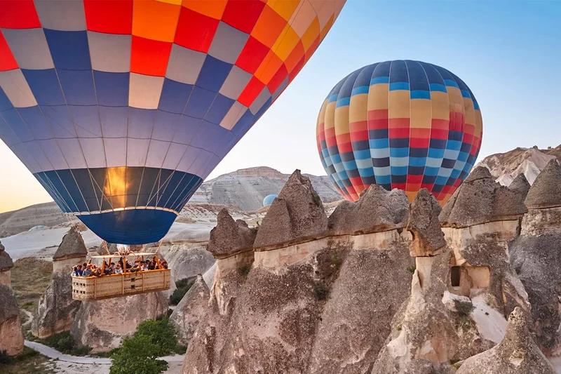 دو بالن هوای گرم رنگارنگ در حال پرواز در ارتفاع پایین بر فراز دودکش های جن در کاپادوکیا