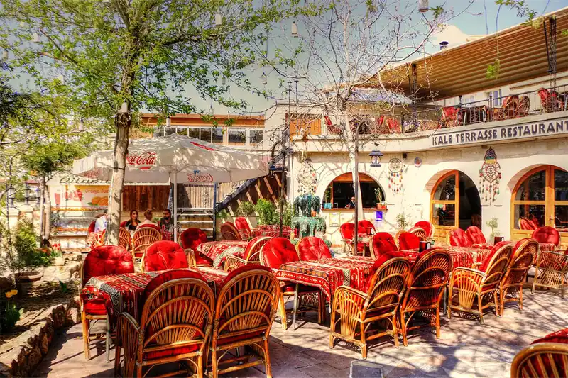 محوطه بیرونی و حیاط آفتاب&zwnj;گیر رستوران سنتی کاله تراس با میز&zwnj; و&zwnj; صندلی&zwnj;های چوبی و رومیزی&zwnj;های قرمز