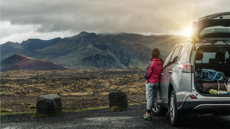 دختری کنار ماشین در حال تماشای منظره