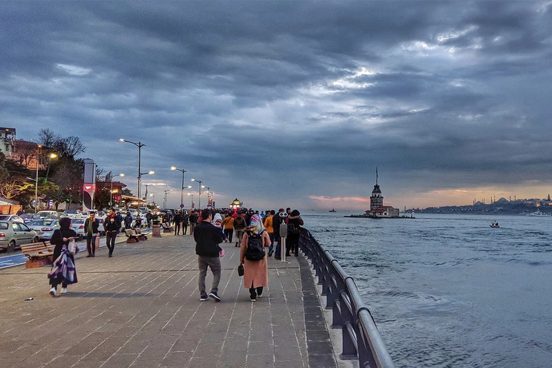 مردم در حال قدم زدن در سواحل اسکودار&nbsp; هنگام غروب، با چشم&zwnj;اندازی از برج دختر